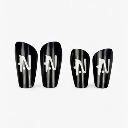 Four black NTMG shin guards with white logo on a white background