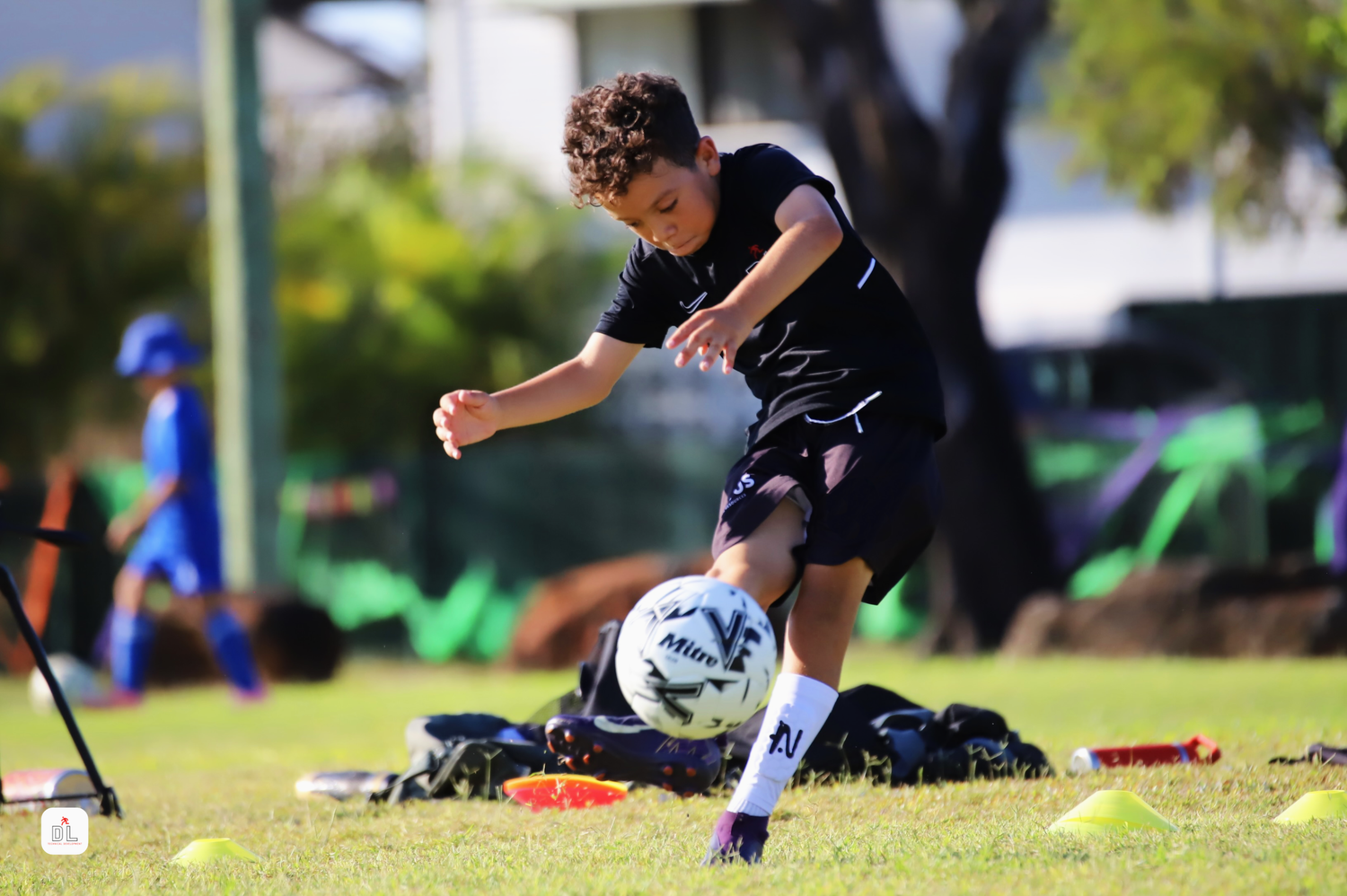 Child playing soccer on a grass field with sports equipment around