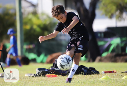 Child playing soccer on a grass field with equipment wearing white NTMG built-in.