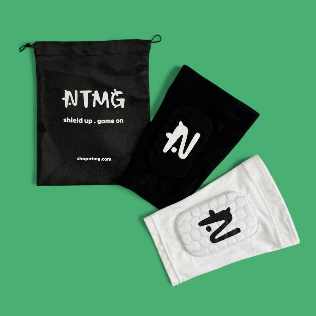Black NTMG carry bag beside black and white NTMG built in shin pads on a green background.