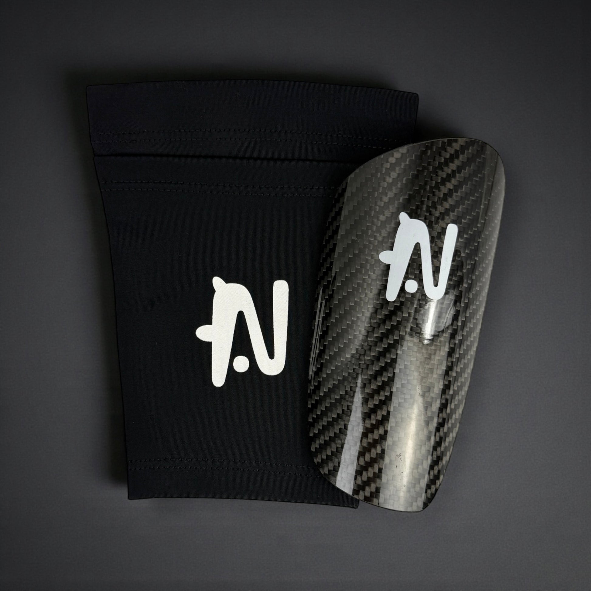 Carbon fiber shin guard with a black sleeve on a dark background