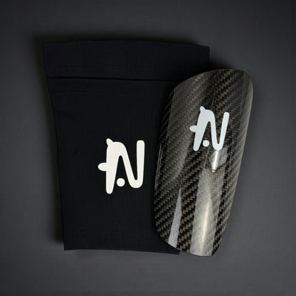 Carbon fiber shin guard with a black sleeve on a dark background