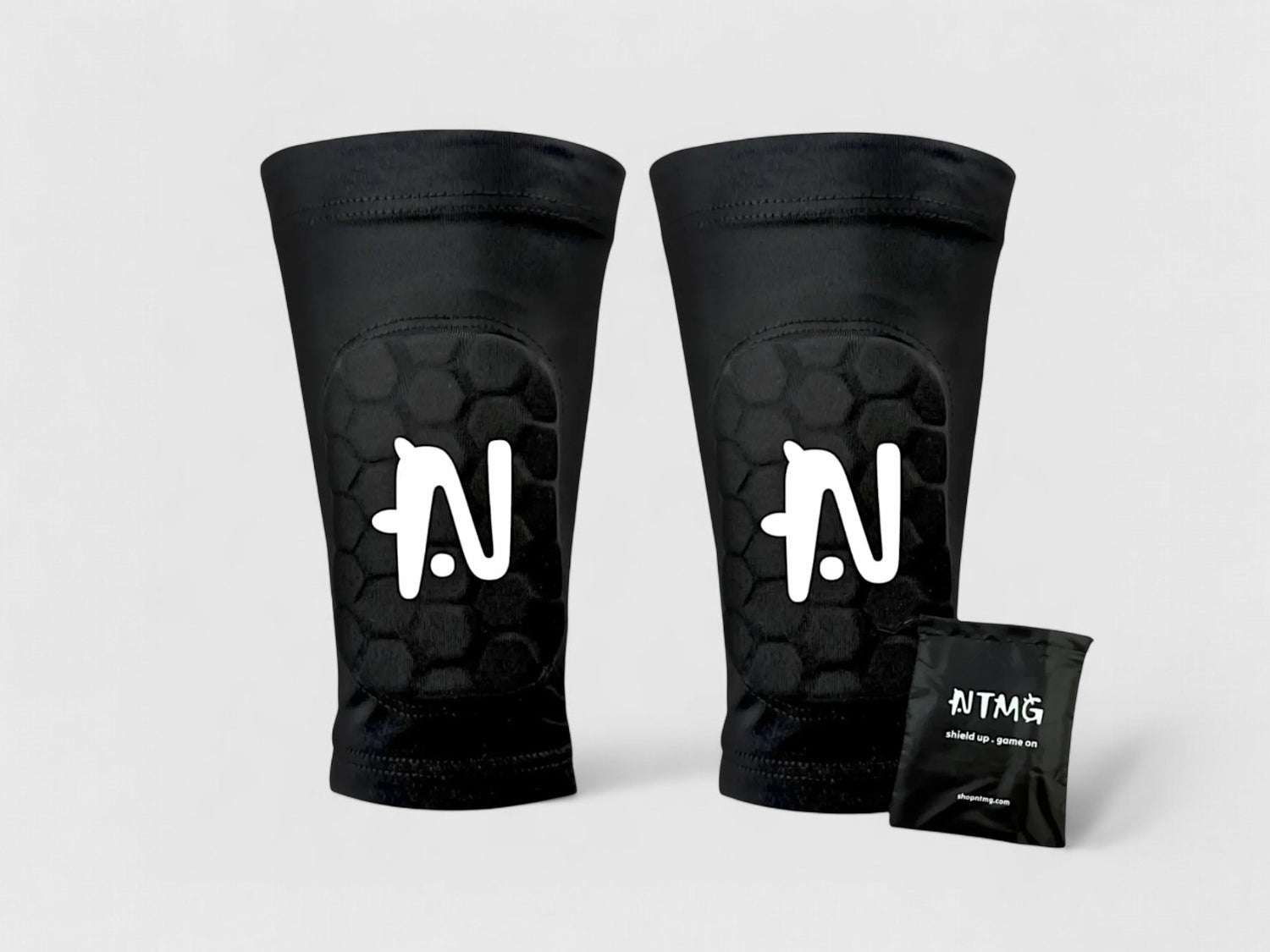 A pair of black NTMG Built-In Shin Pads  with their bag on a light gray background