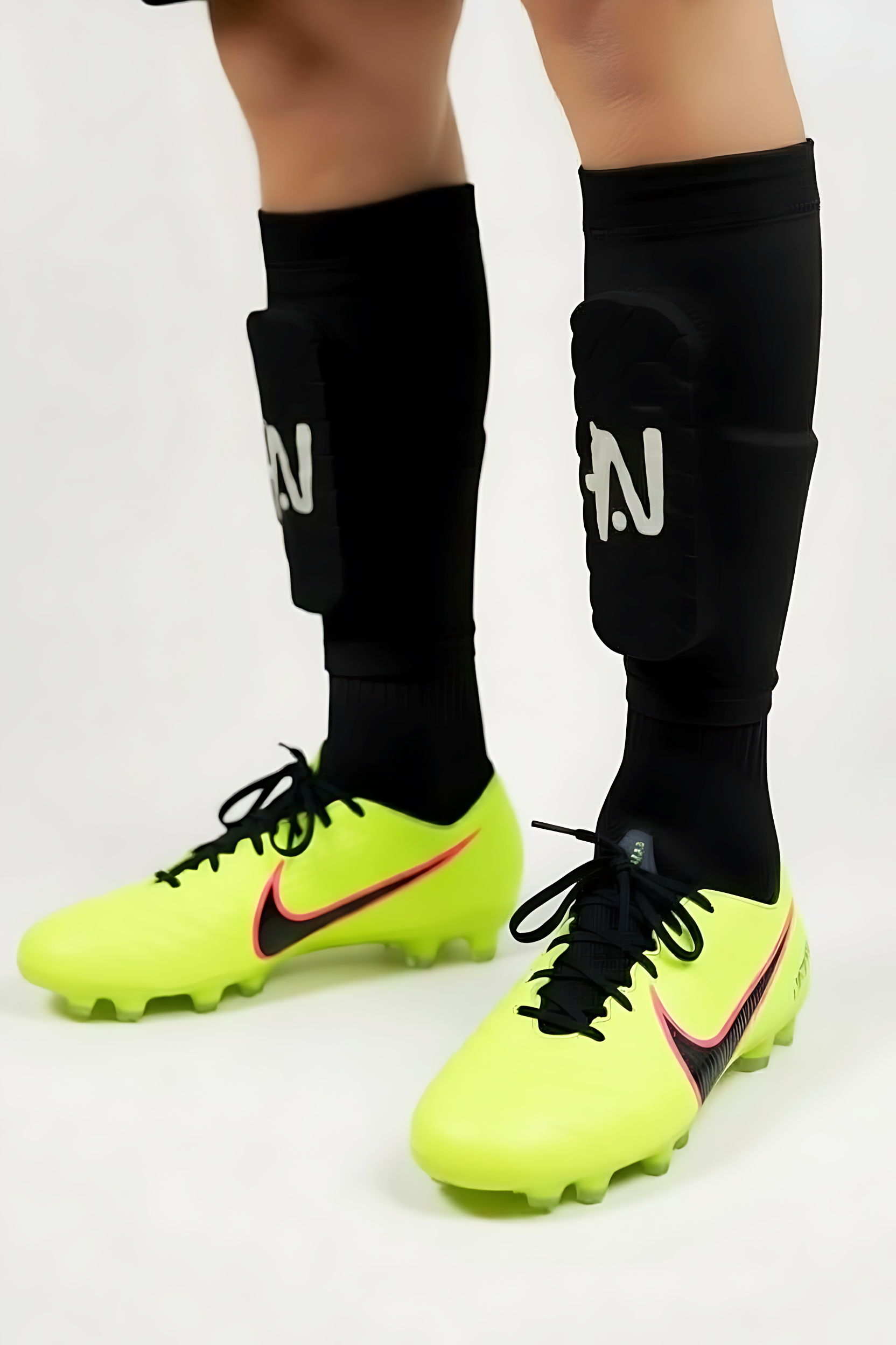 Yellow soccer cleats with black NTMG built in shin guards on a white background